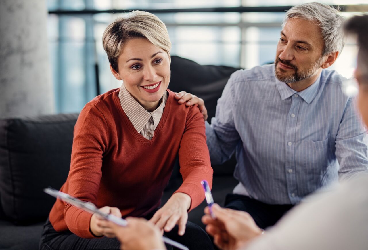 Smiling couple meeting with a healthcare professional to review insurance coverage for Cigna drug rehab treatment options.